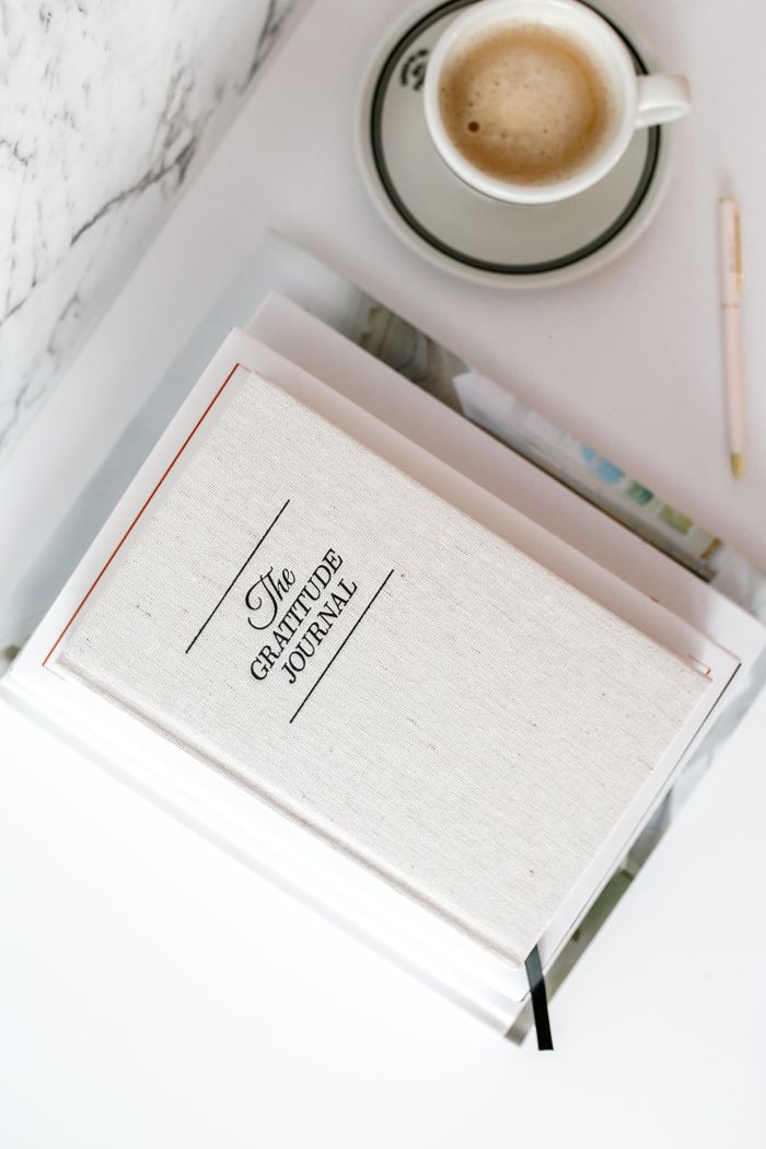 A gratitude journal and coffee cup on a white desk create a serene workspace vibe.