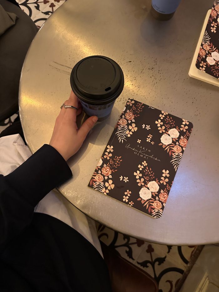 A cozy scene with a coffee cup and floral notebook on a café table.